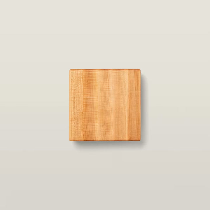 A square wooden cutting board with a natural light brown grain, centered on a light beige background.