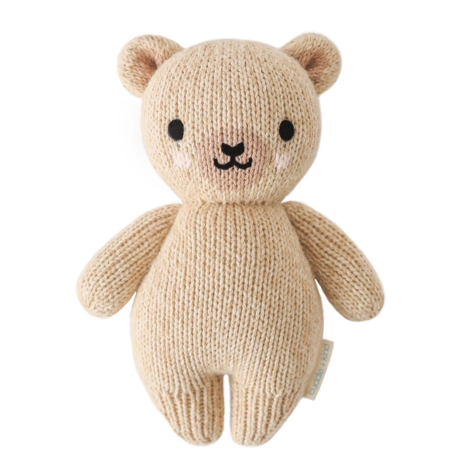 A beige knitted teddy bear plush toy with black embroidered eyes, nose, and mouth