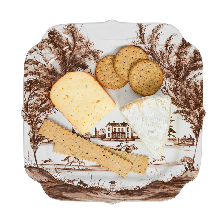 Decorative plate with a landscape design featuring cheese, crackers, and bread.
