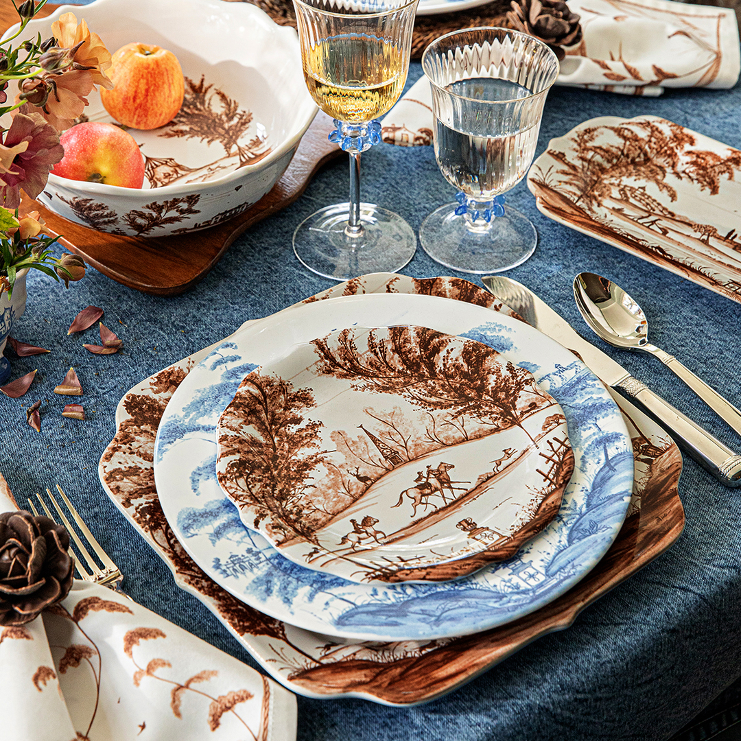Set table with decorative plates, glasses, and cutlery on a blue tablecloth.