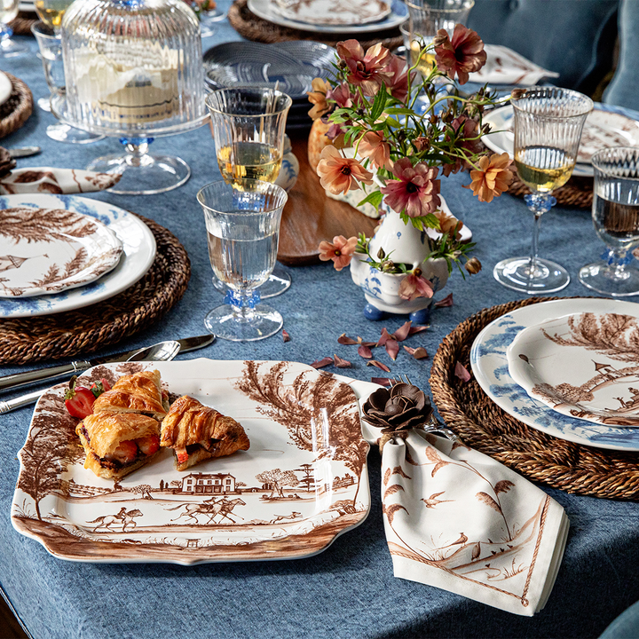Elegant table setting with floral centerpiece, plates, and glasses on a blue tablecloth.