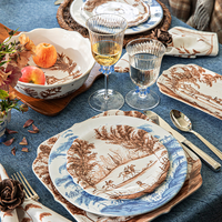 Decorative table setting with patterned plates, glasses, and cutlery on a blue tablecloth.