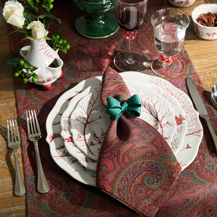 Dining table setting with patterned napkin, plates, and cutlery on a decorative tablecloth.