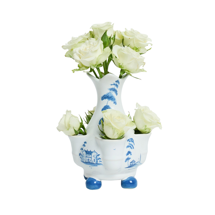 A white ceramic three-bowl flower vase with blue hand-painted landscape motifs and blue feet, filled with white roses