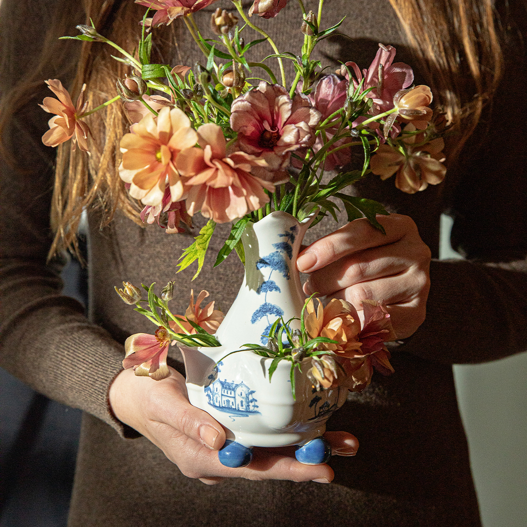 Person holding a white vase with floral design and flowers.