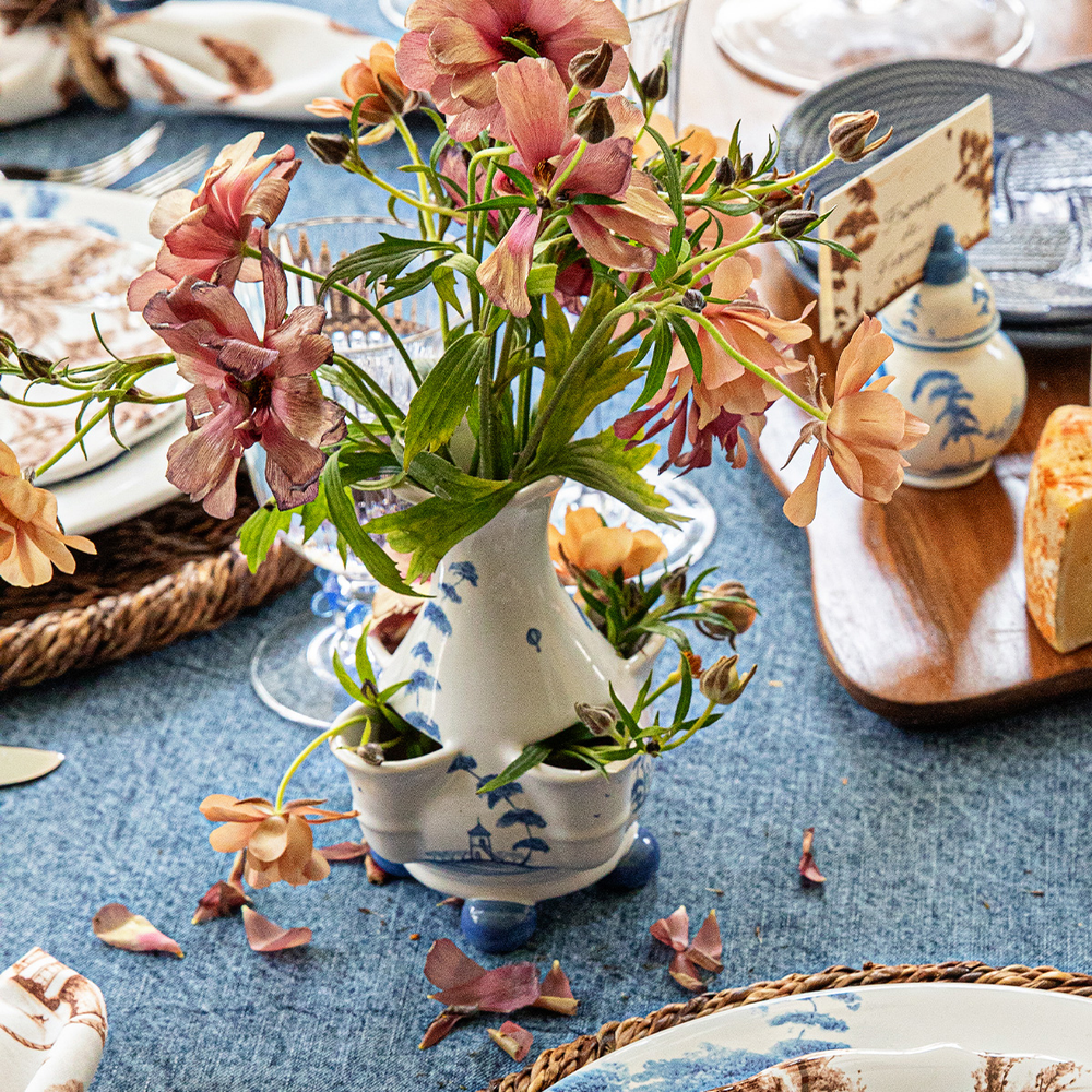 Decorative table setting with flowers in a ceramic pitcher on a blue tablecloth.