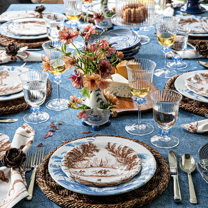 Elegant table setting with floral centerpieces, glassware, and patterned plates on a blue tablecloth.