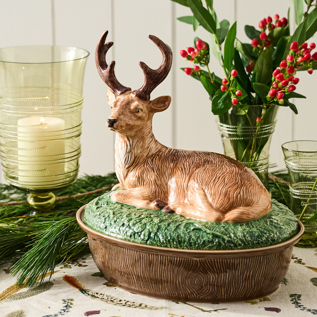 Decorative deer figurine on a green cushion with candles and flowers in the background.