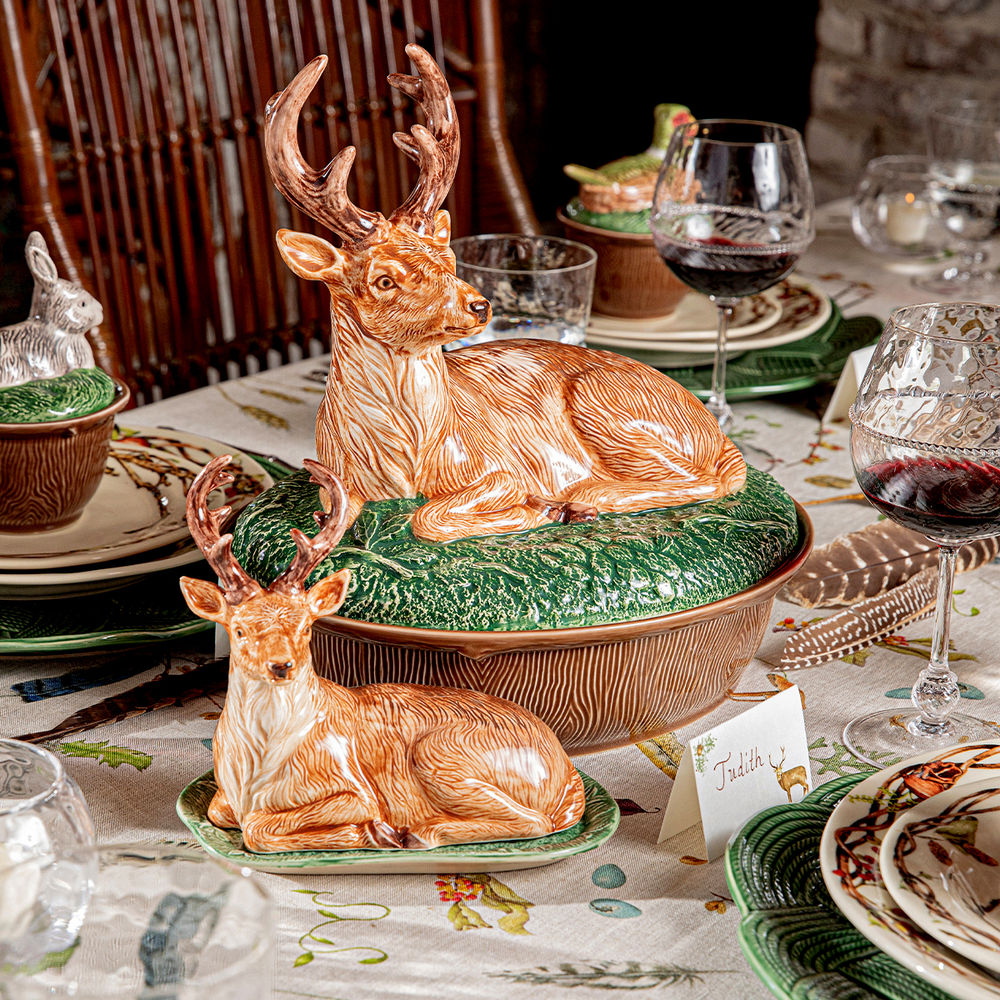 Decorative ceramic deer figures on a table with wine glasses and place cards.