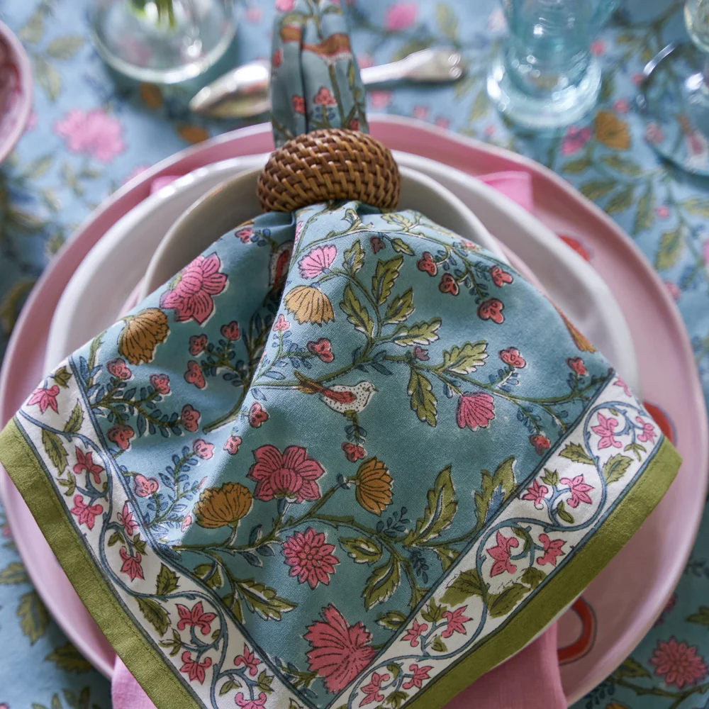 blue, orange, pink, and green Floral-patterned napkin on a pink plate with a decorative holder on a tablecloth.