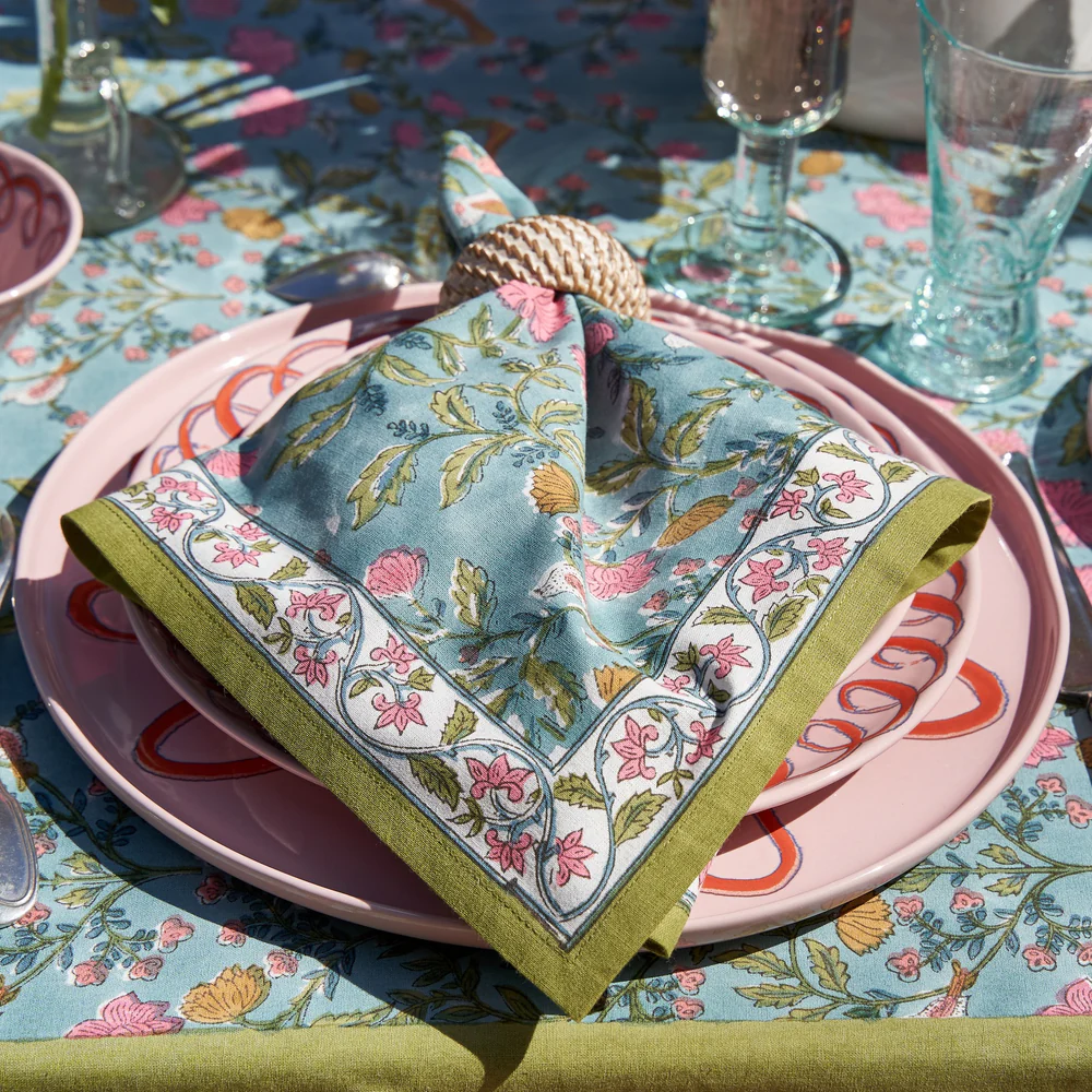 Decorative table setting with floral napkin and plates on a patterned tablecloth.