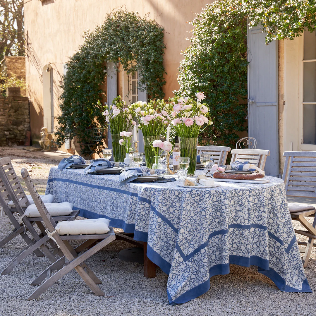 Outdoor table setting with a floral tablecloth and chairs in a garden.
