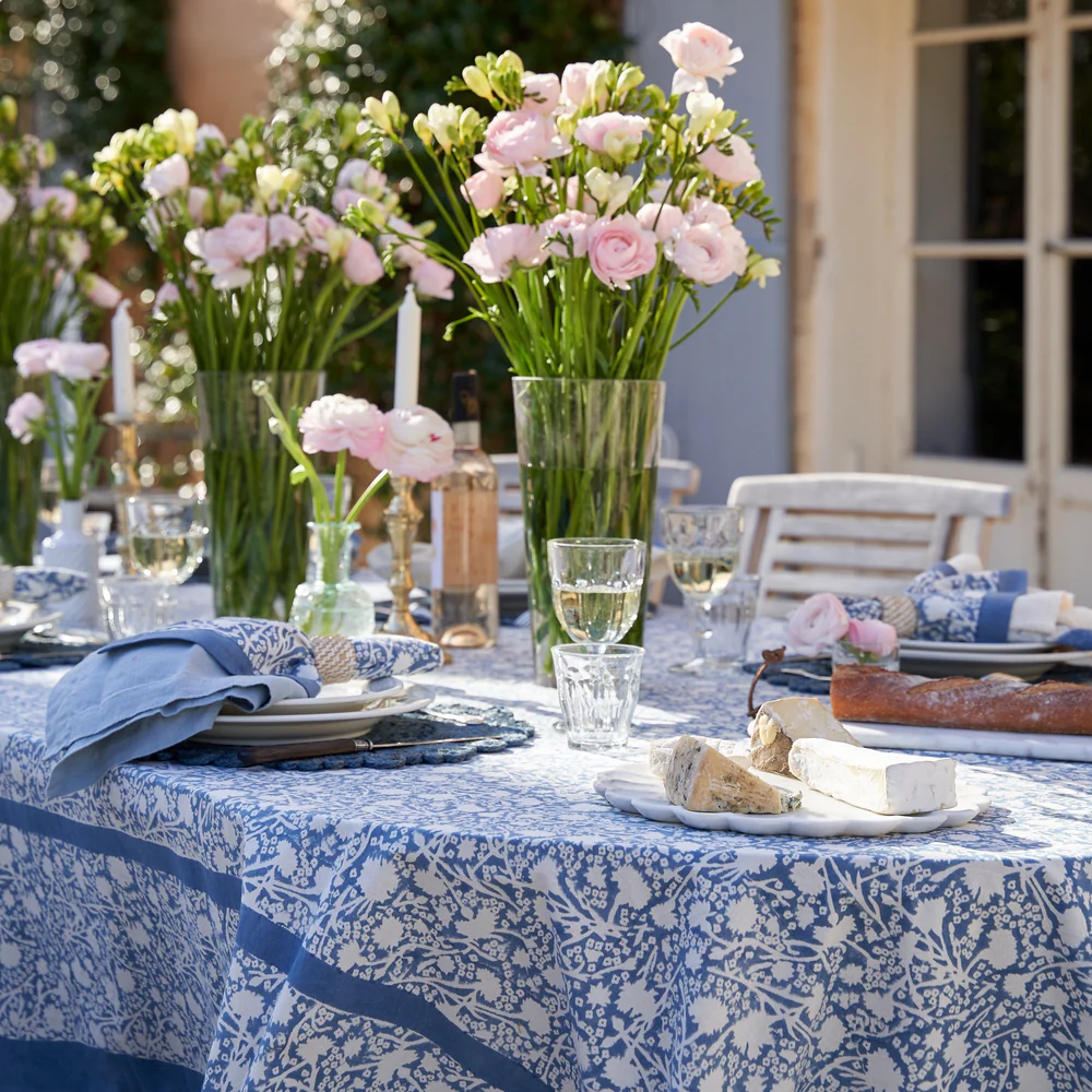 Outdoor table setting with floral arrangements and blue and white tablecloth