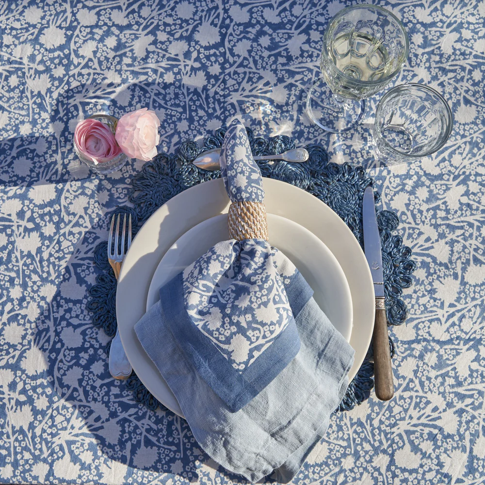 Table setting with blue and white floral tablecloth, plates, cutlery, and napkins.