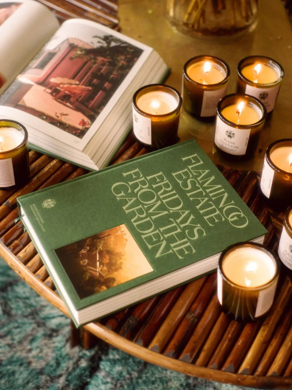 Green book titled 'Flamingo State Fridays from the Garden' on a wooden table with lit candles.