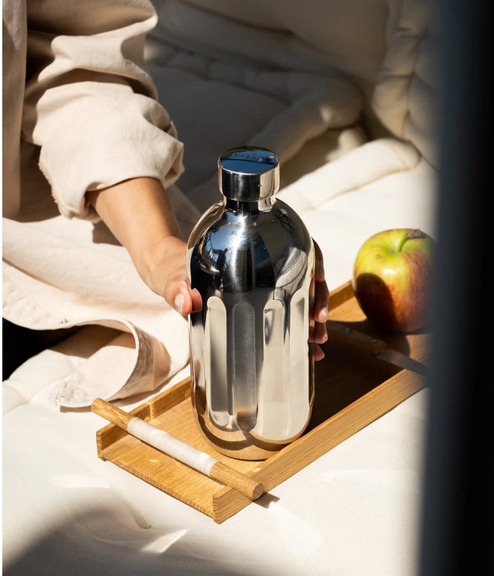Person holding a silver soda bottle on a wooden tray with an apple in the background