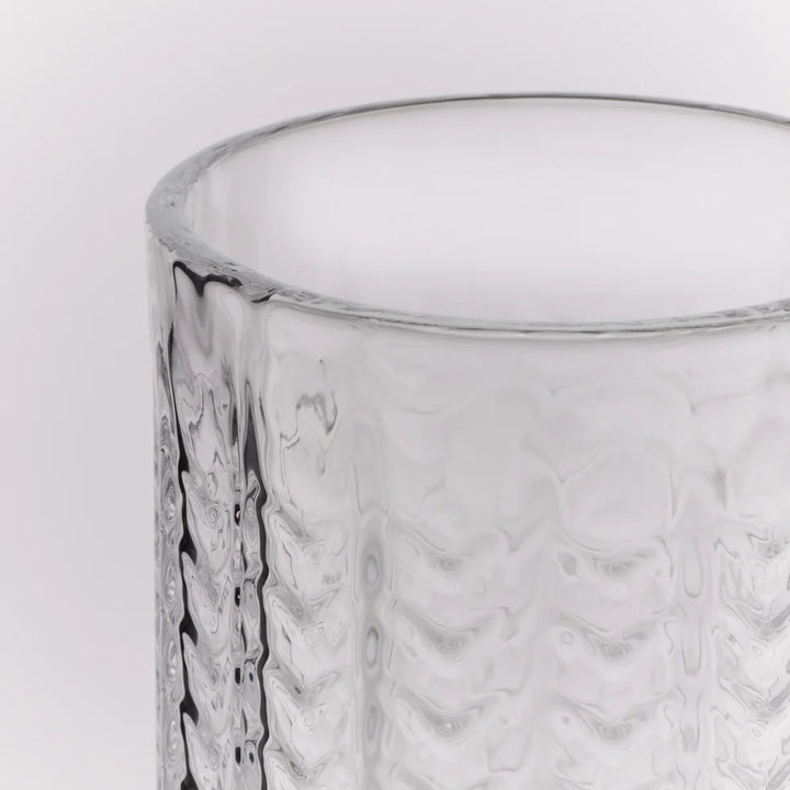 A close-up of a clear textured glass tumbler with a wavy pattern, shown against a plain white background.