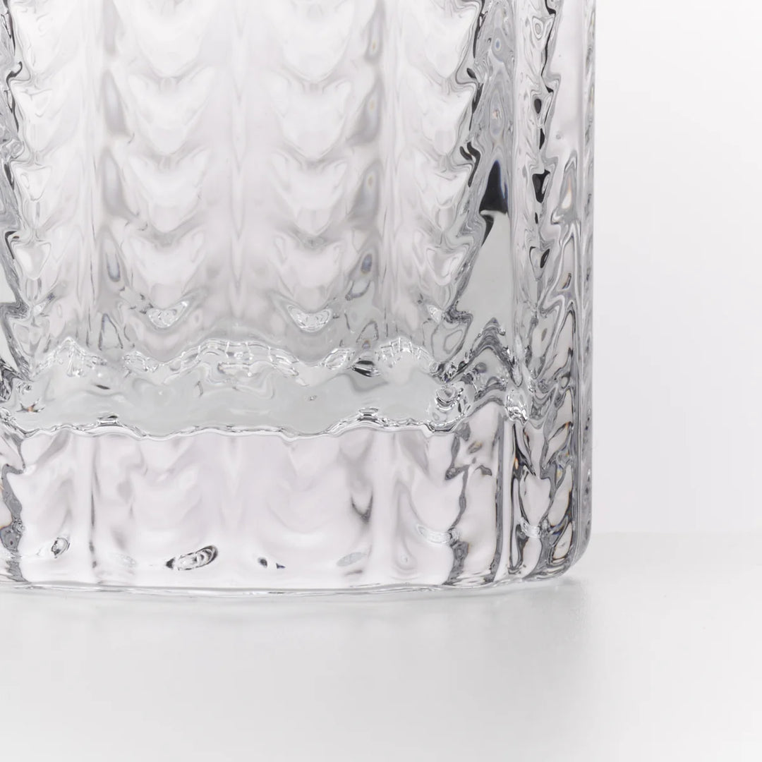 A close-up of a clear textured glass tumbler showing the wavy pattern on the side and a flared, ribbed base against a white background.