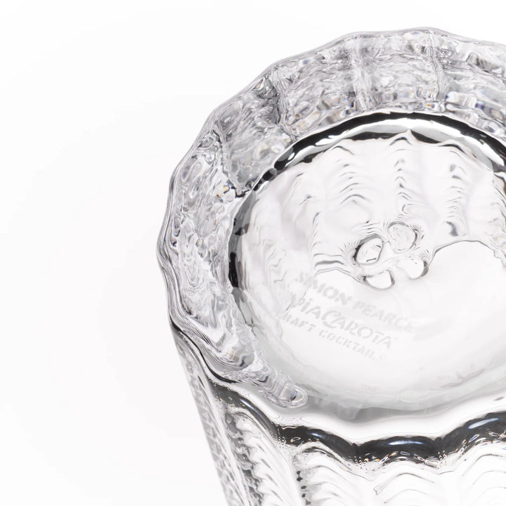 A close-up of a clear textured glass tumbler, showing the inside base engraved with 'SIMON PEARLS MACARONET CRAFT COCKTAILS' on a white background.