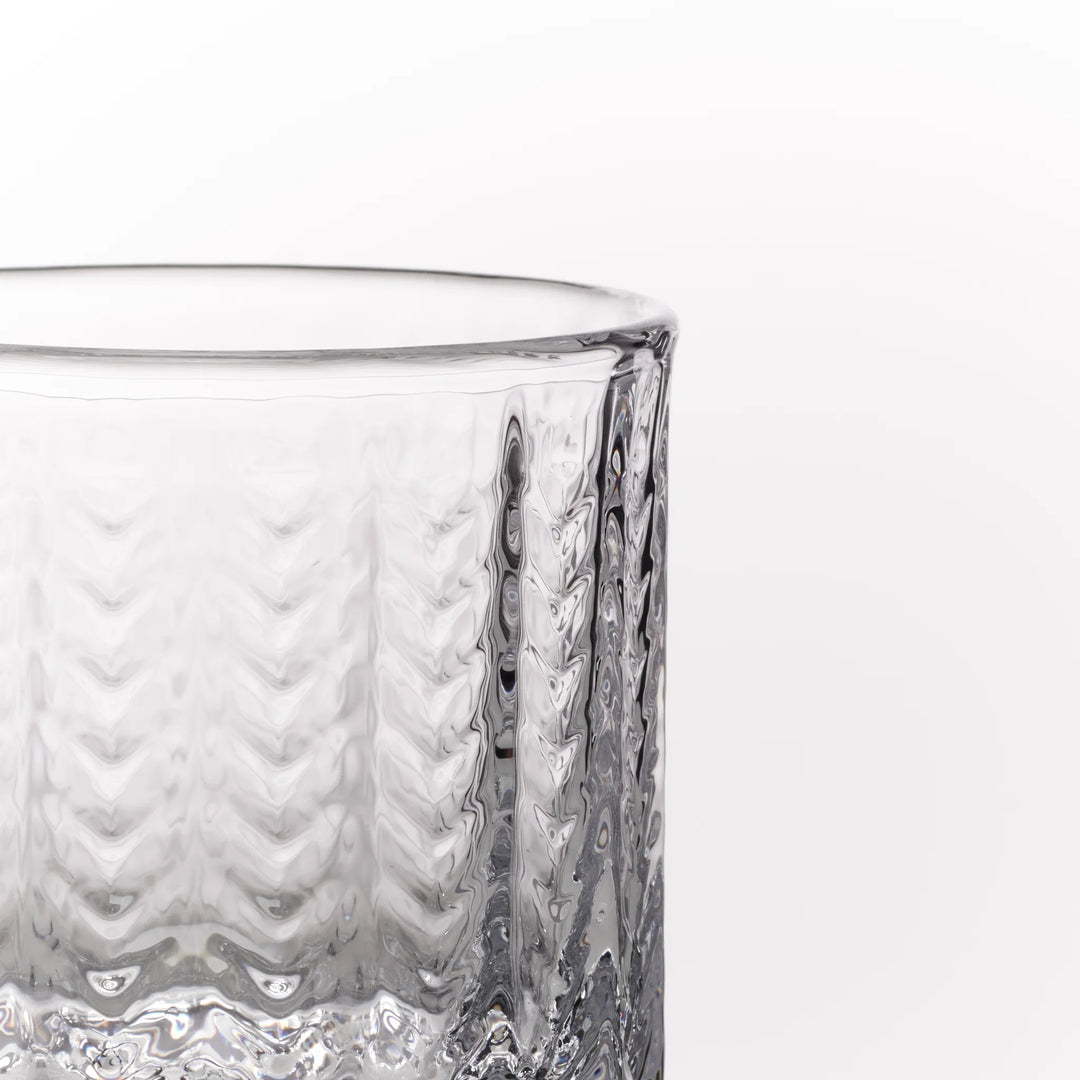 A close-up of a clear textured glass tumbler showing its ribbed pattern against a plain white background.