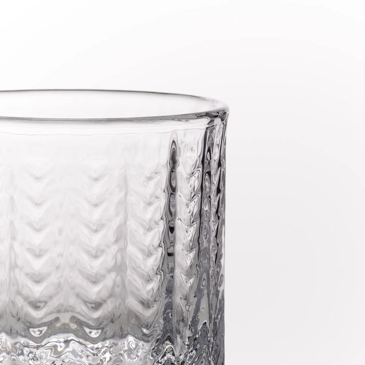 A close-up of a clear textured glass tumbler showing its ribbed pattern against a plain white background.