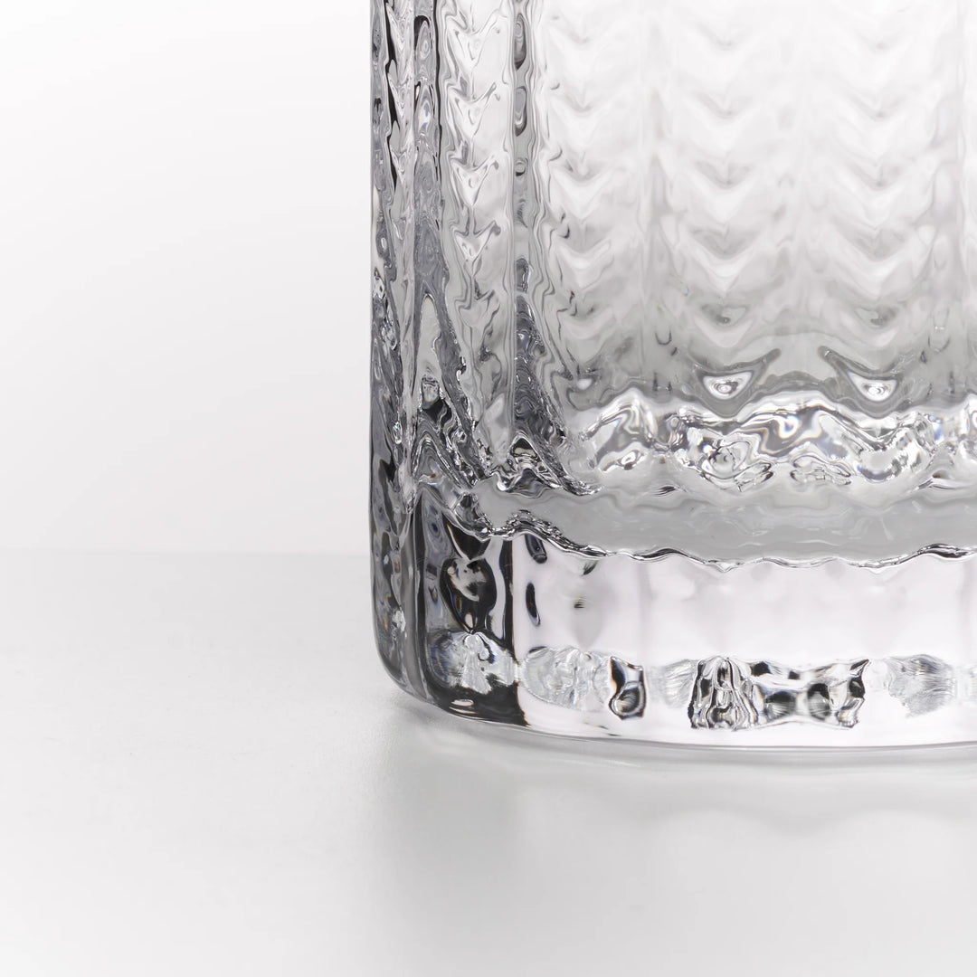 Close-up of a clear textured glass tumbler with a wavy, hammered pattern and a thick scalloped base, shown on a clean white background.