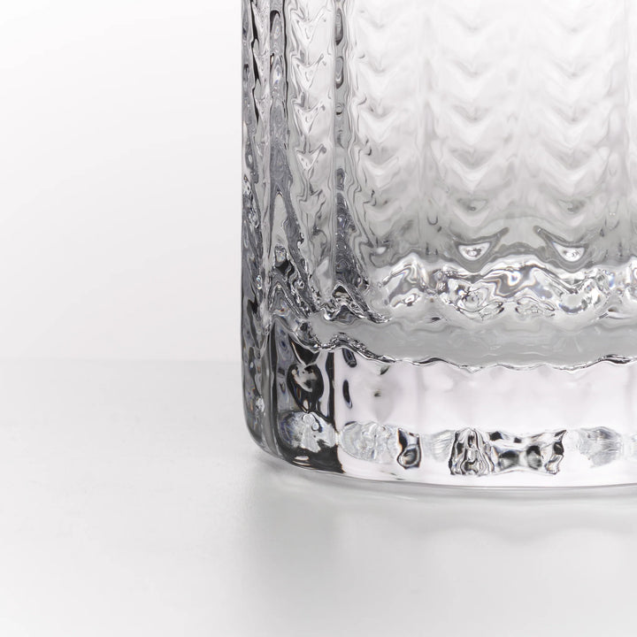 Close-up of a clear textured glass tumbler with a wavy, hammered pattern and a thick scalloped base, shown on a clean white background.