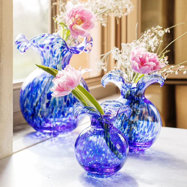 Blue glass speckled vases with floral arrangements sitting by a window