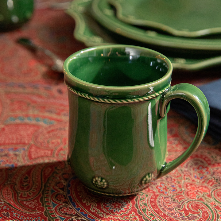 Green ceramic mug with decorative handle on a patterned tablecloth