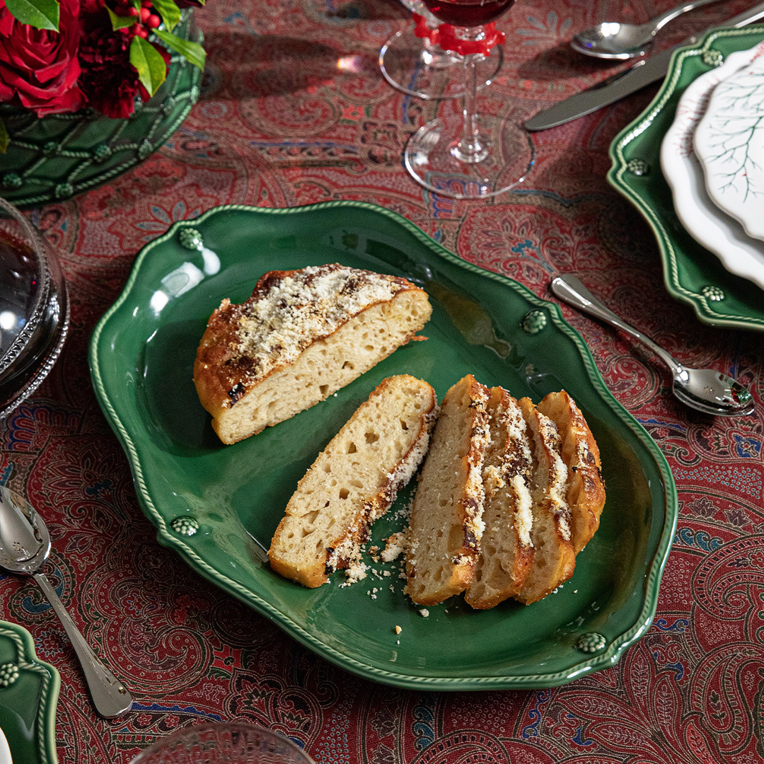 Three slices of bread on a green plate with a patterned tablecloth and glasses 