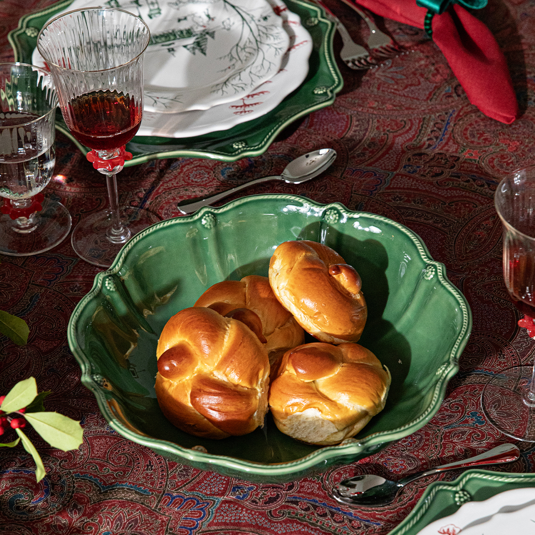 Green bowl with bread rolls on a festive table setting with wine glasses and holly.