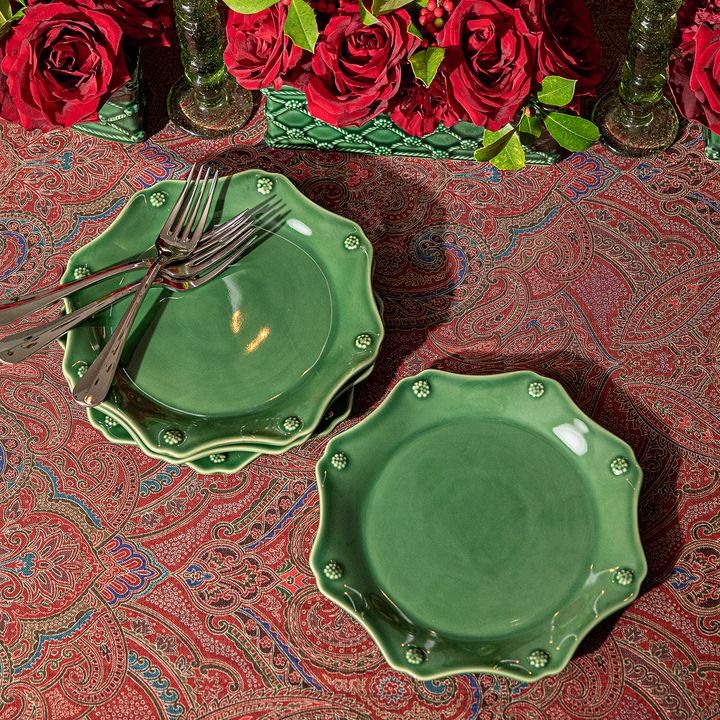 Green ceramic plates with decorative edges on a patterned red tablecloth with red roses.