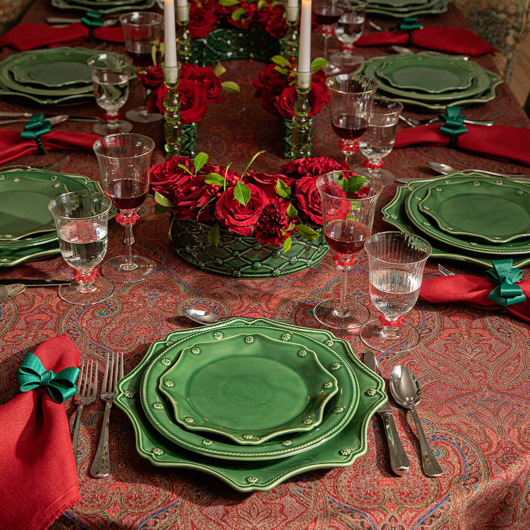 Dining table set with green plates, red napkins, and red roses on a patterned tablecloth.