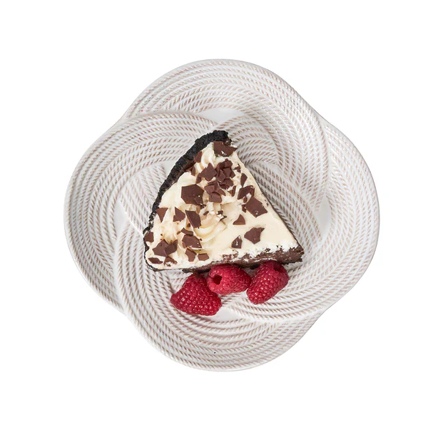 white plate with knot designs with a cheese cake topped with chocolate shavings garnished with raspberries