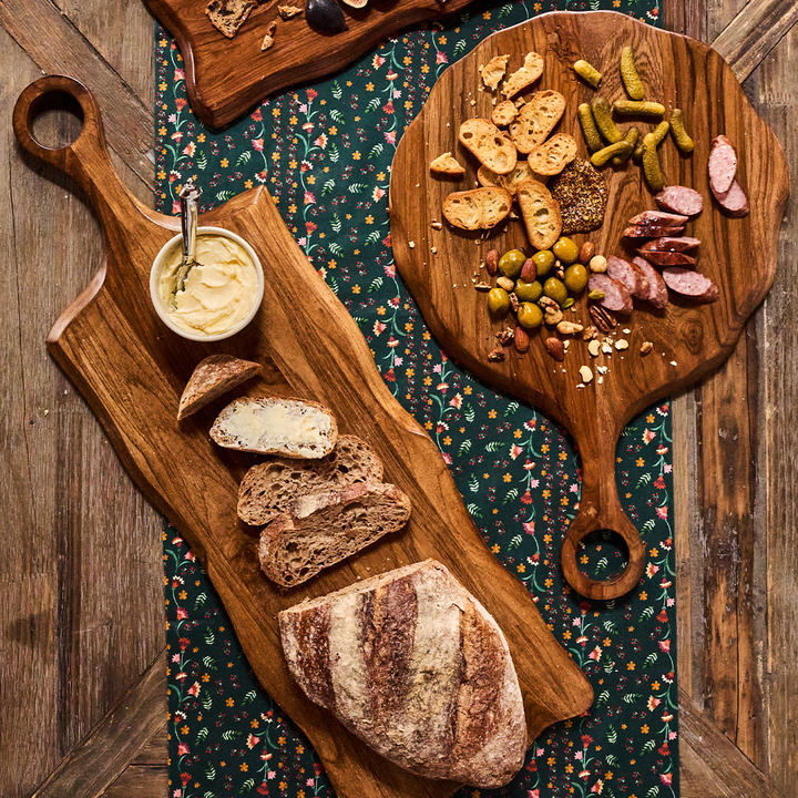 Wooden platters with bread, meats, and cheeses on a patterned tablecloth.
