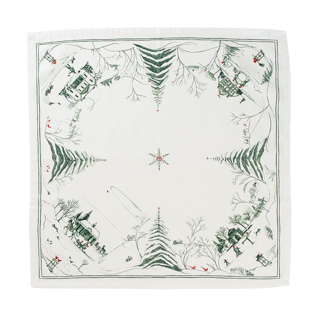 A square white fabric napkin featuring a winter village scene printed in dark green and small red accents, with pine trees, cabins, and a star motif in the center.