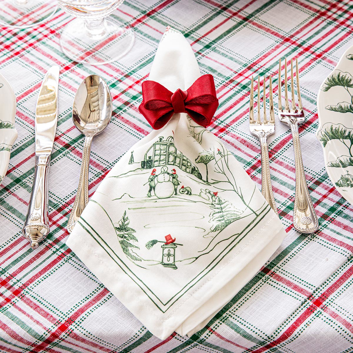 Christmas-themed place setting with a decorative napkin and cutlery on a plaid tablecloth.