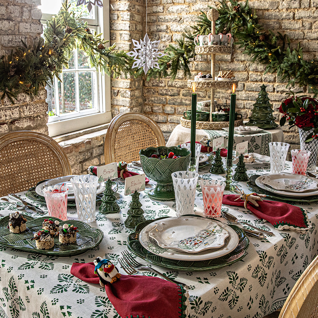 Decorative Juliska Christmas table setting with greenery and candles in a rustic room.