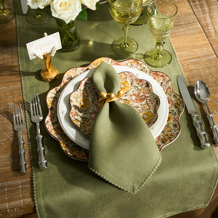 Elegant table setting with green napkin tied with a gold acorn napkin ring, decorative fall plates, and cutlery on a wooden table.