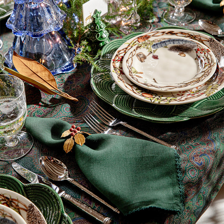 Decorative table setting with green napkin, patterned plates, and silverware on a textured tablecloth.