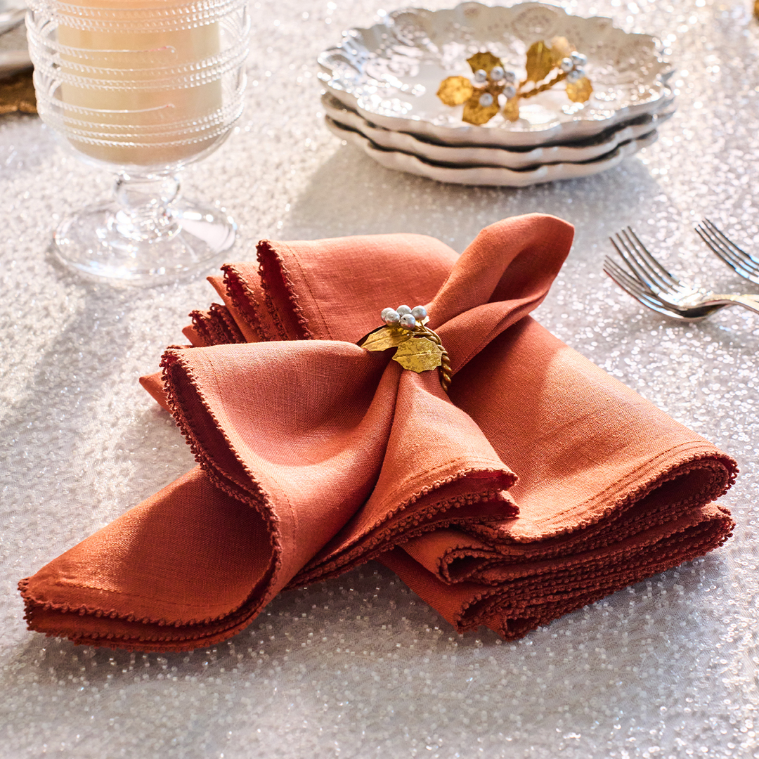 Folded orange napkin with a decorative gold leaf on a sparkling tablecloth.