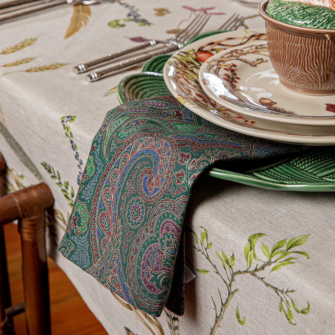 Decorative table setting with a paisley napkin, plates, and cutlery on a patterned tablecloth.