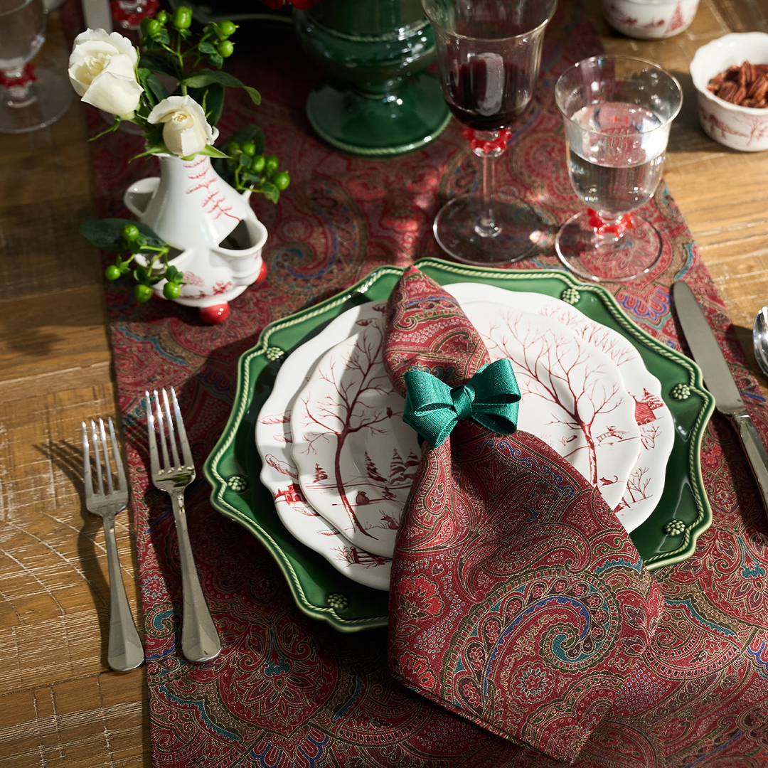 Dining table setting with decorative plates, napkin, and cutlery on a patterned tablecloth.