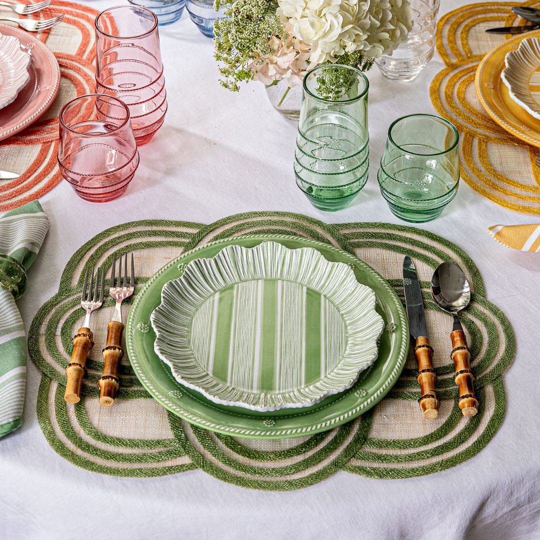 Decorative table setting with green plates, glasses, and cutlery on a white tablecloth.