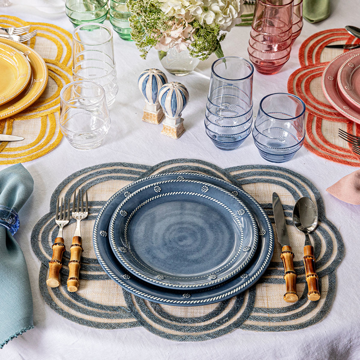 Dining table setting with blue berry and thread plates, cutlery, and colorful placemats.