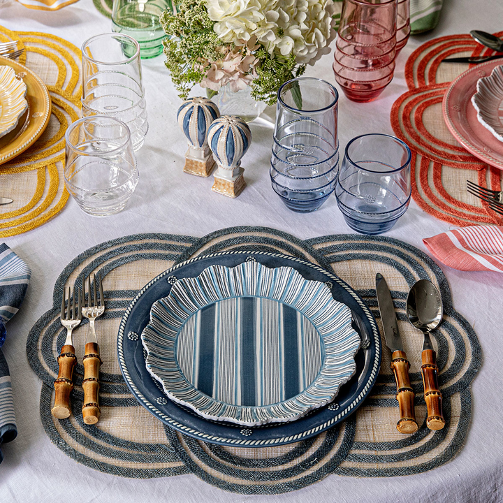 Dining table setting with blue striped plates, glasses, and cutlery on a patterned placemat.