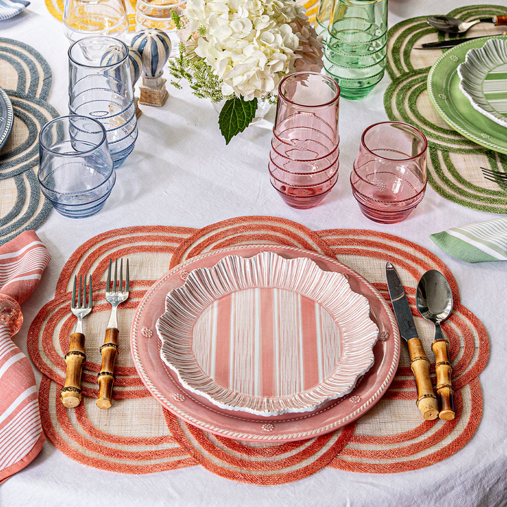 Dining table setting with pink striped plates, glasses, and cutlery on a white tablecloth.