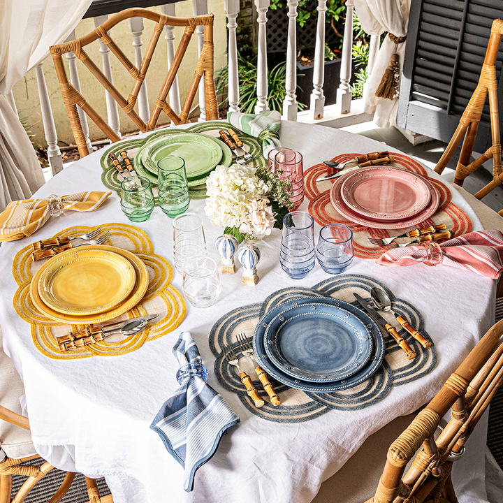 Dining table set with colorful plates, glasses, and cutlery on a white tablecloth.
