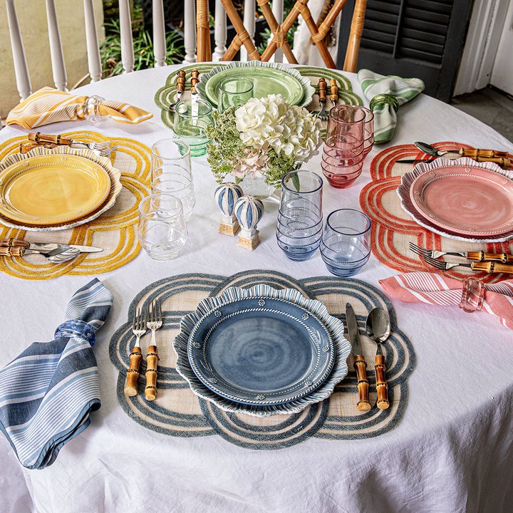 Colorful table setting with patterned plates and placemats on a white tablecloth.