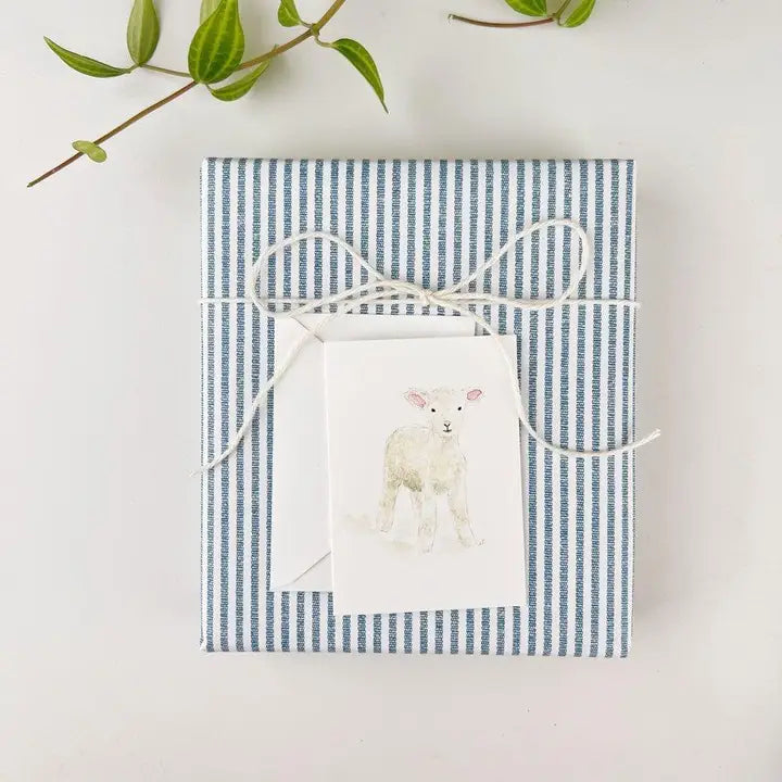 Gift box with blue and white striped paper and a white card featuring a lamb illustration on a light gray background.